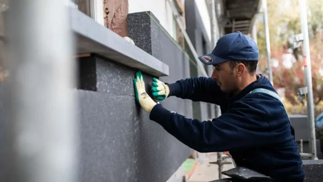 Ouvrier Isolution posant un panneau isolant sur une façade par l'extérieur à Wavre