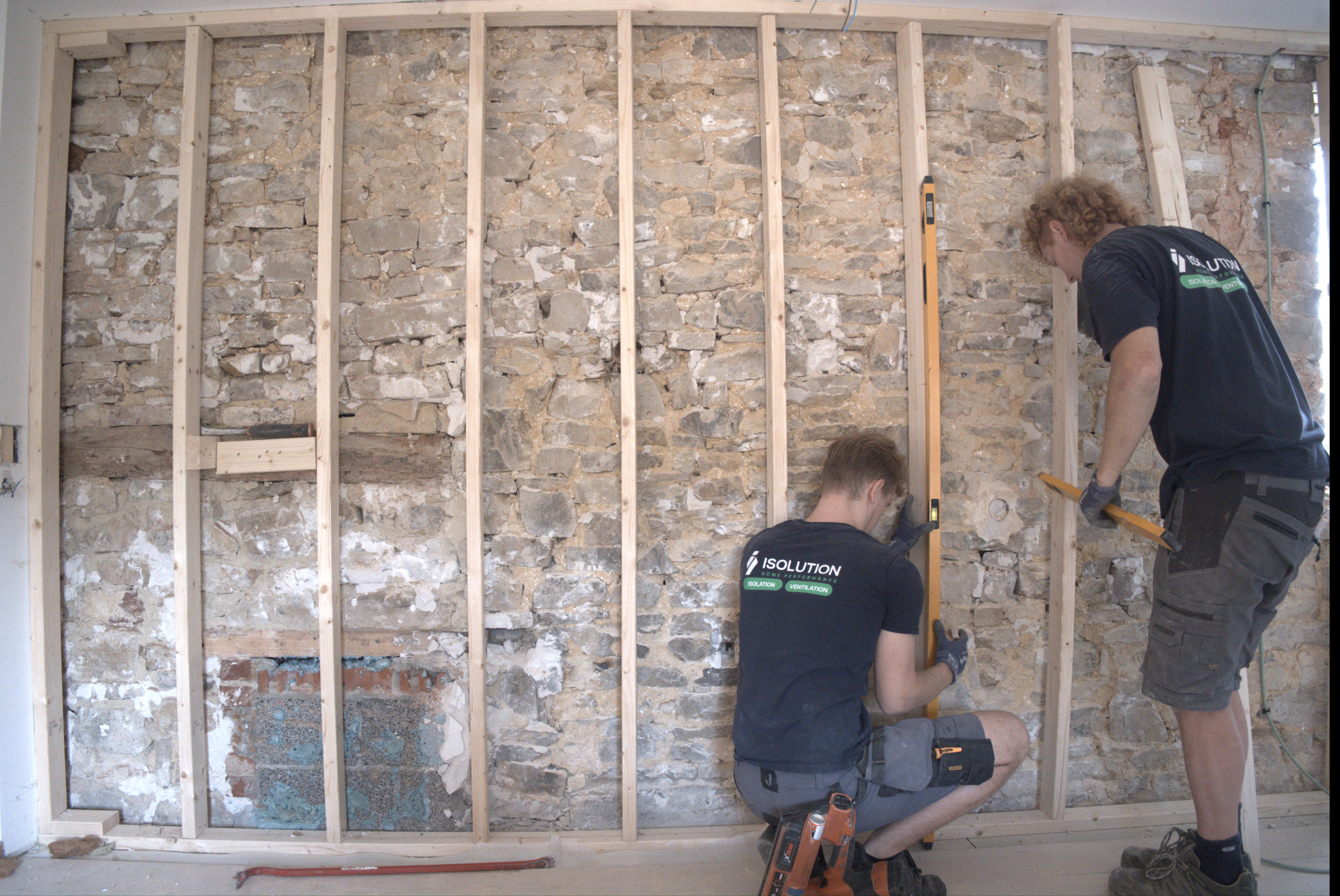Deux techniciens ISOLUTION posent une ossature en bois sur un mur intérieur en pierres pour une isolation par l'intérieur