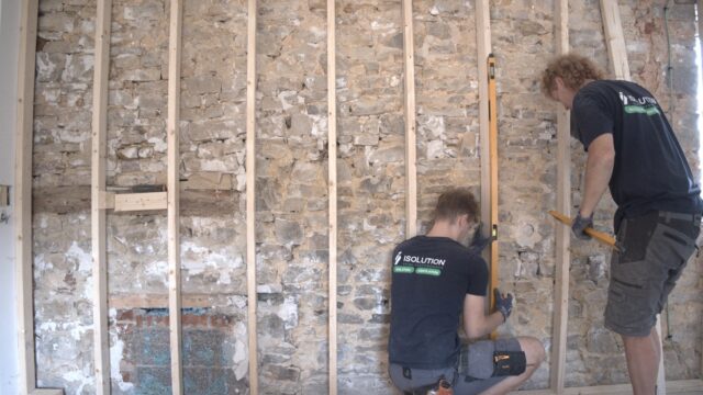 Deux techniciens ISOLUTION posent une ossature en bois sur un mur intérieur en pierres pour une isolation par l'intérieur