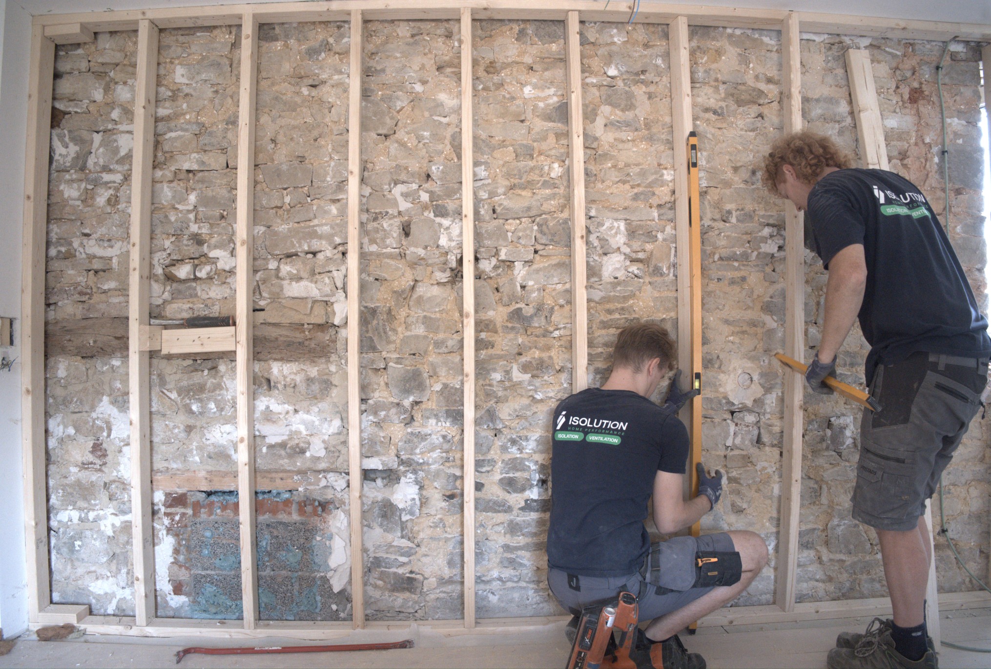 Deux techniciens ISOLUTION posent une ossature en bois sur un mur intérieur en pierres pour une isolation par l'intérieur